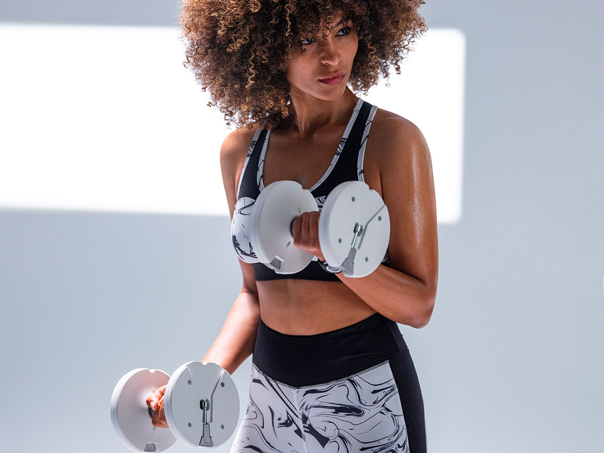 Woman lifting 25lb white adjustable dumbbells from T9 series during a home workout session