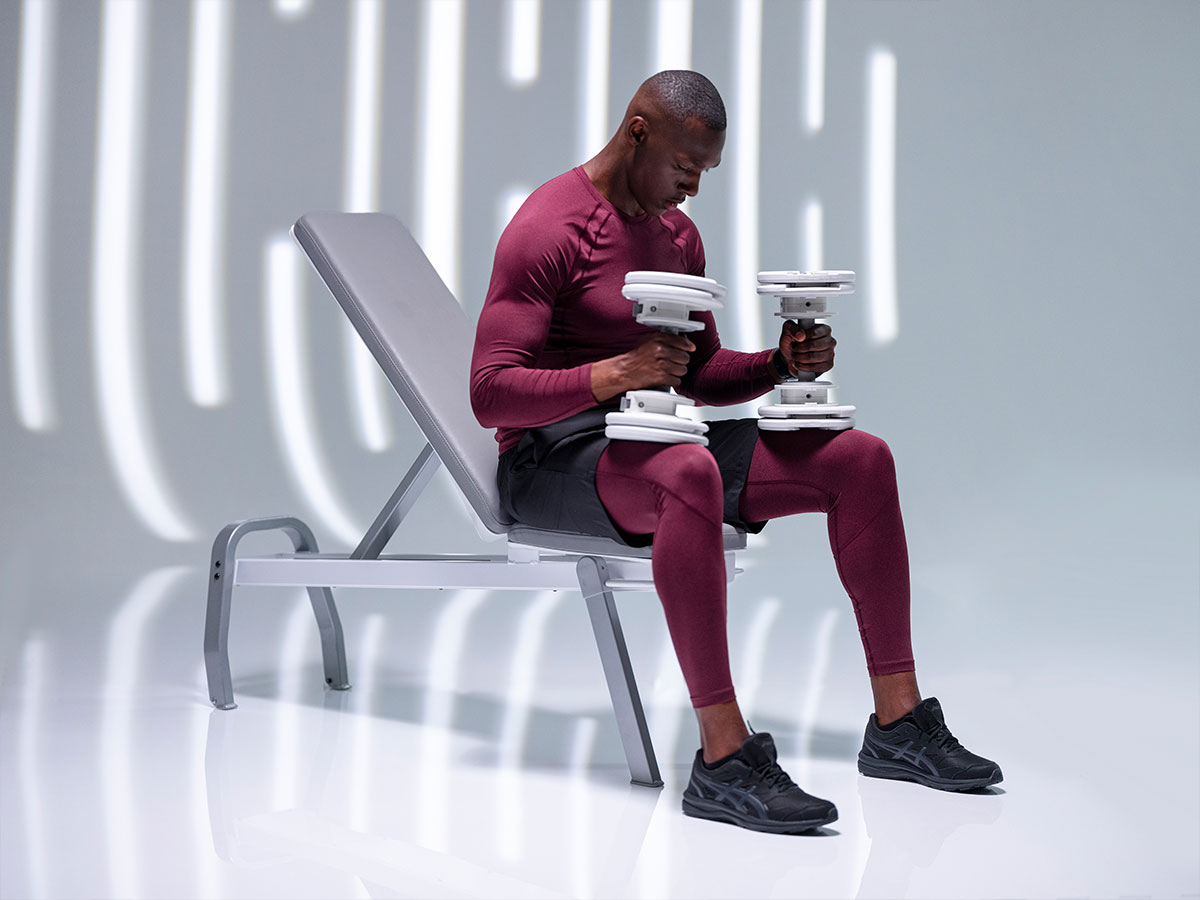 Man performing strength exercises with a white adjustable 55lb dumbbell from the T9 Series on a bench.