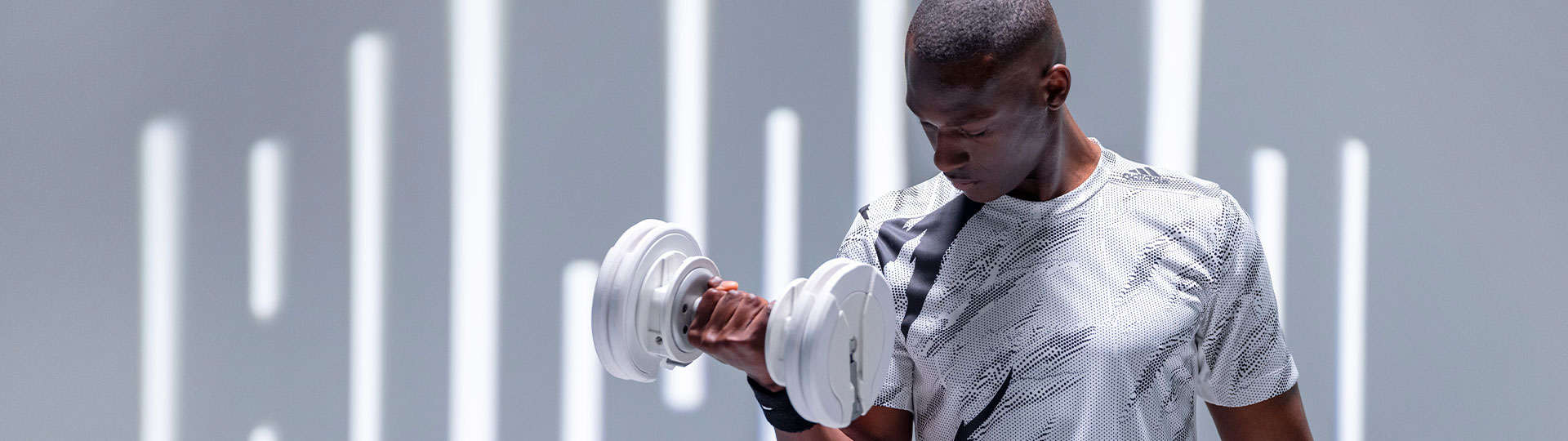 Man lifting a white adjustable 55lb dumbbell from the T9 Series in a modern gym.