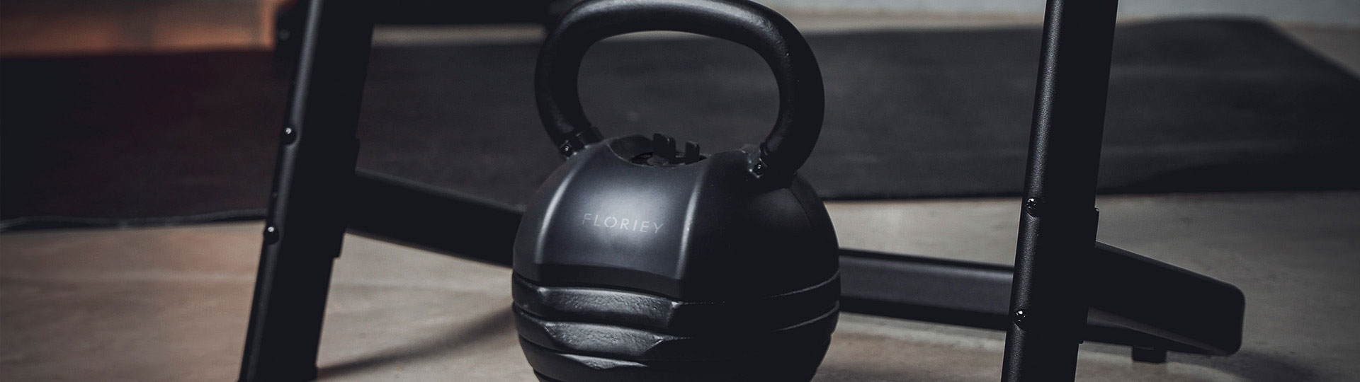 Close-up of the 50lb black adjustable kettlebell under gym equipment.
